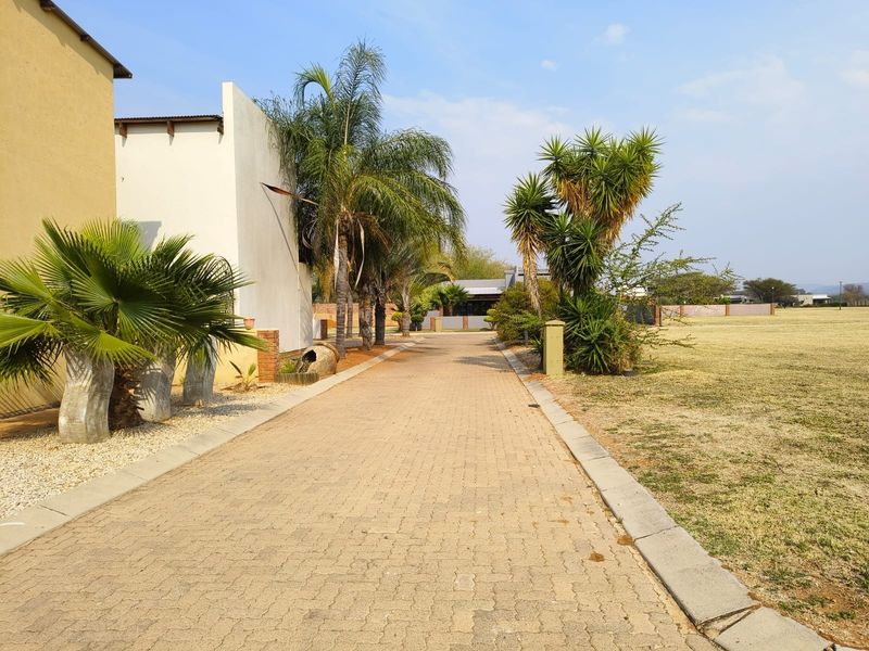 A well-maintained paved driveway leading towards the property, flanked by established palm trees and open lawn areas.