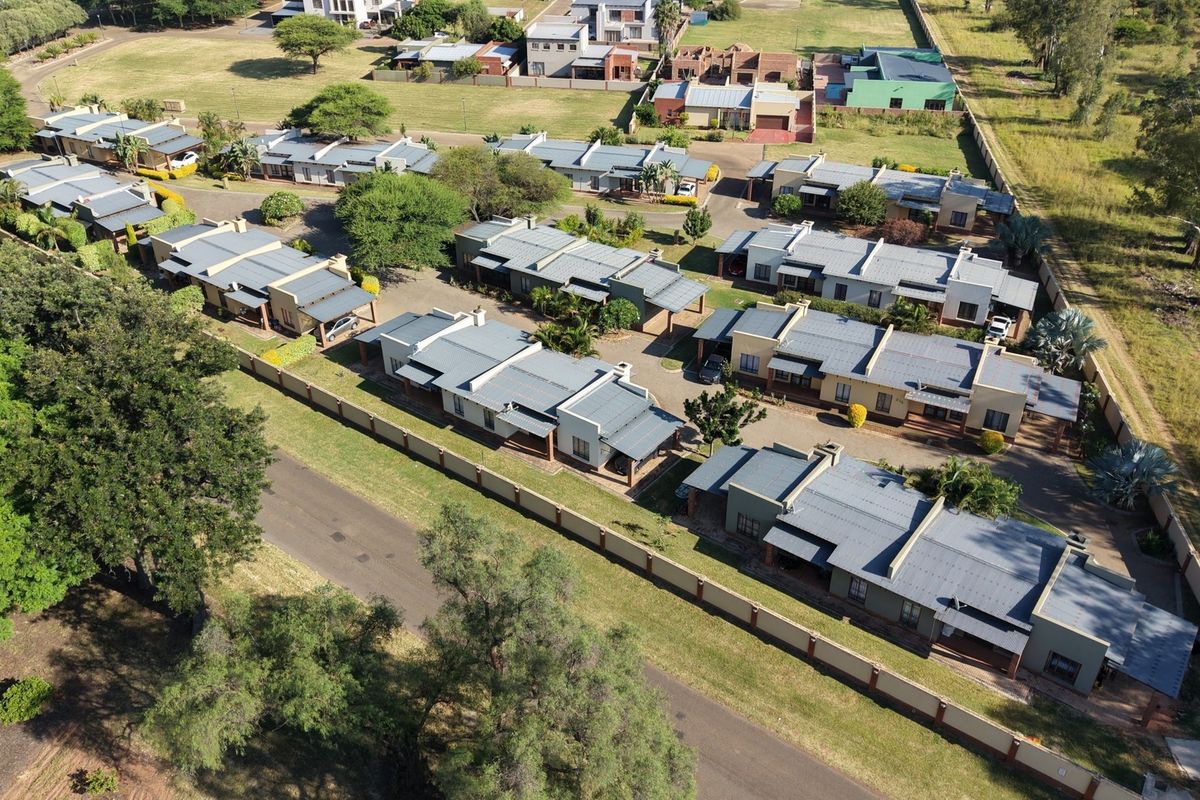 Aerial view of a residential complex featuring multiple housing units with metal roofs, paved access roads, and perimeter walling.