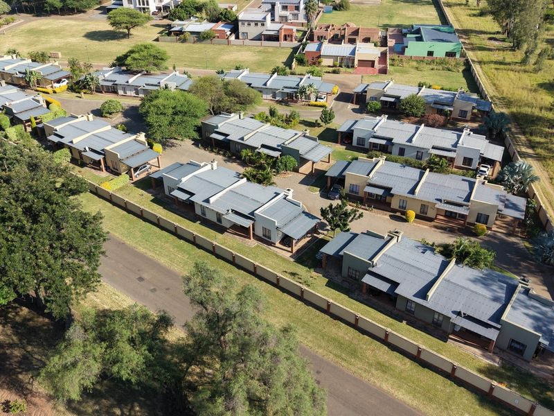Aerial view of a residential complex featuring multiple housing units with metal roofs, paved access roads, and perimeter walling.