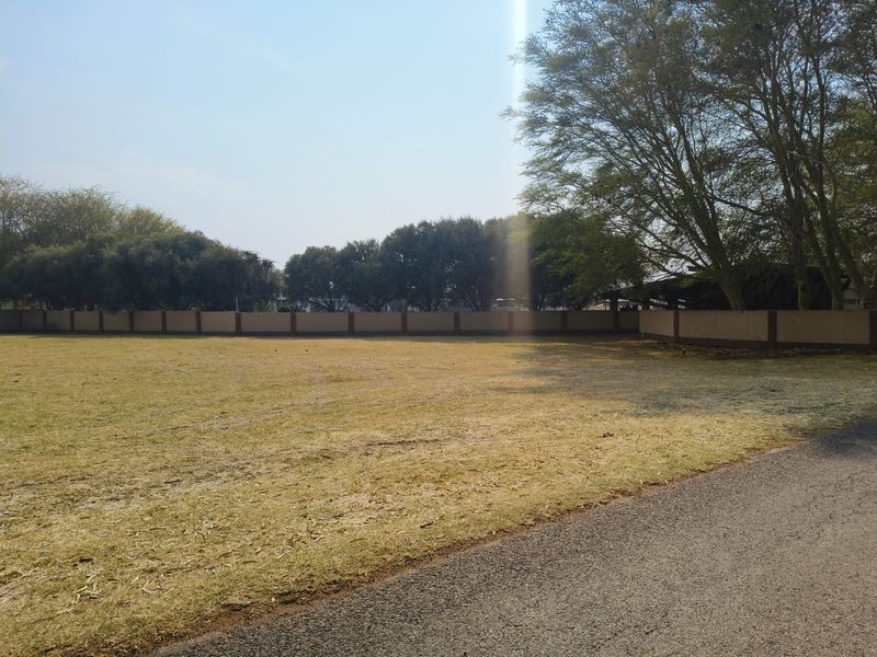 A vacant residential plot featuring a level grassed area, perimeter boundary wall, and adjacent asphalt driveway access.
