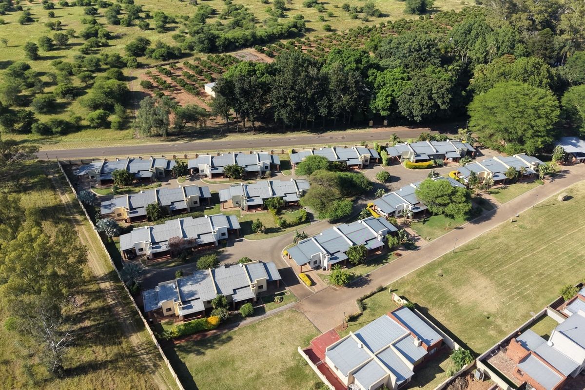 Aerial view of a residential complex featuring multiple housing units, paved internal roads, and surrounding landscaped grounds.