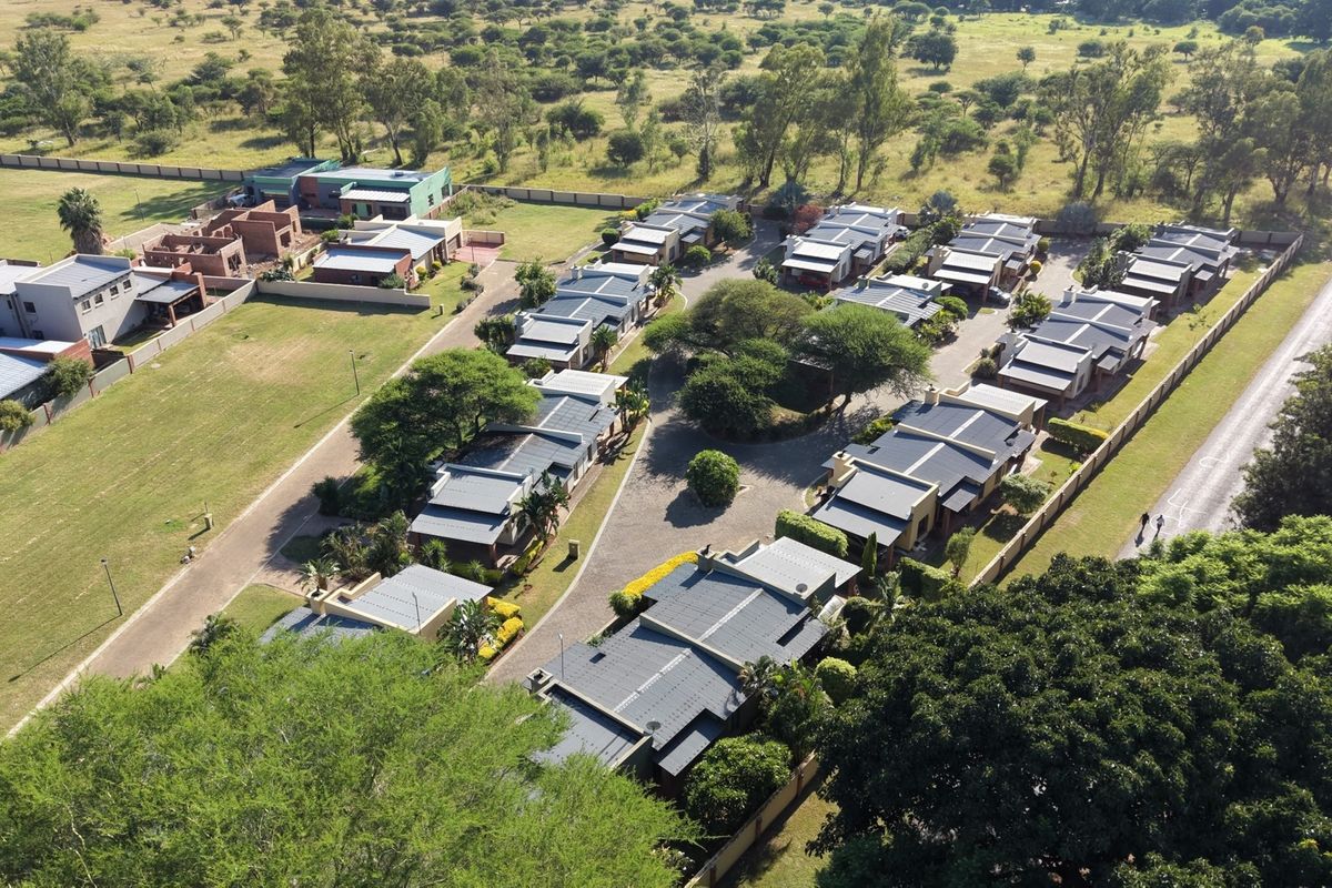 An aerial view of a residential estate featuring multiple housing units, paved internal roads, and established landscaping within a secure perimeter.