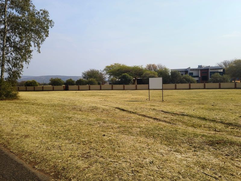 A vacant residential plot featuring a level grass surface, enclosed by a perimeter wall and boundary fencing.