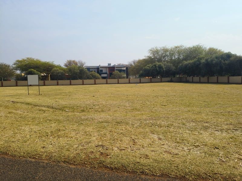 A vacant residential plot featuring a level grass lawn enclosed by a perimeter wall, offering a clear space for future development.