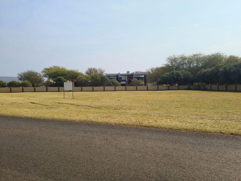 A vacant residential plot featuring a level grassed area, enclosed by a perimeter wall, with direct access from an asphalt road.