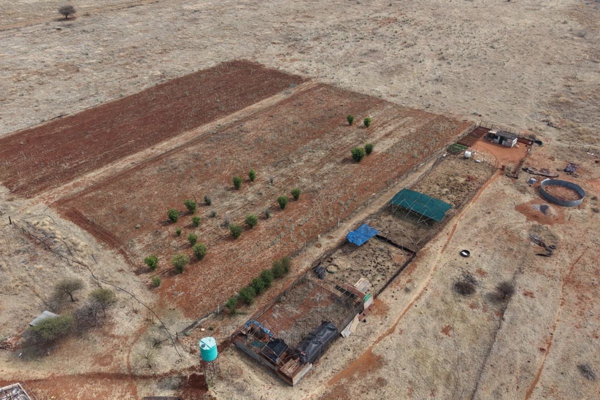 Aerial view of a farm property featuring cultivated land, livestock enclosures, shade structures, and a water tank.