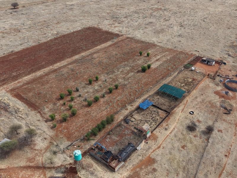 Aerial view of a farm property featuring cultivated land, livestock enclosures, shade structures, and a water tank.