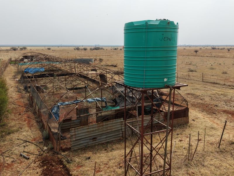 Aerial view of a farm utility area featuring a large water storage tank on a metal stand and a dilapidated metal frame structure.