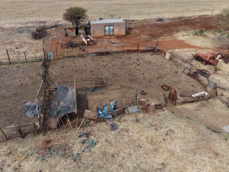 Aerial view of a rural farm property featuring a fenced enclosure and a small, weathered outbuilding structure set within a dry landscape.