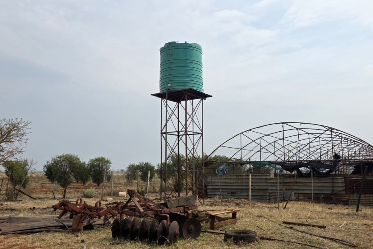 Farm exterior featuring a raised water tank on a steel stand and a dilapidated metal-framed structure with corrugated cladding.