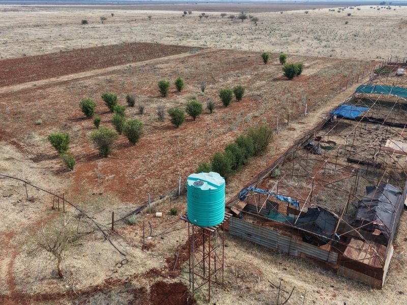 Aerial view of a farm property featuring an orchard, a raised water tank on a metal stand, and several agricultural shade structures.