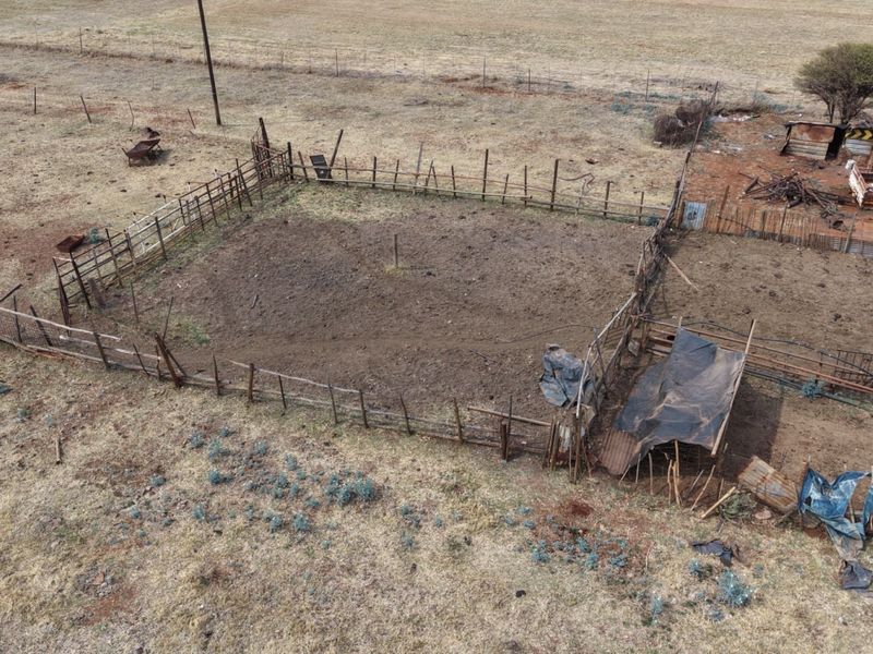 Aerial view of a farm enclosure featuring wire fencing, wooden posts, and a small corrugated iron shelter structure on dry land.