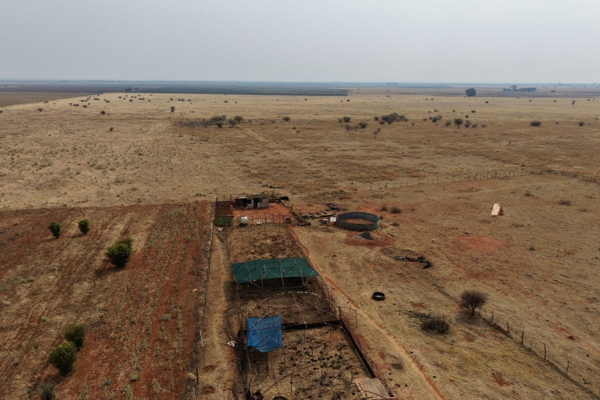 Aerial view of a large farm property featuring expansive open grazing land, agricultural enclosures, and a circular water reservoir.
