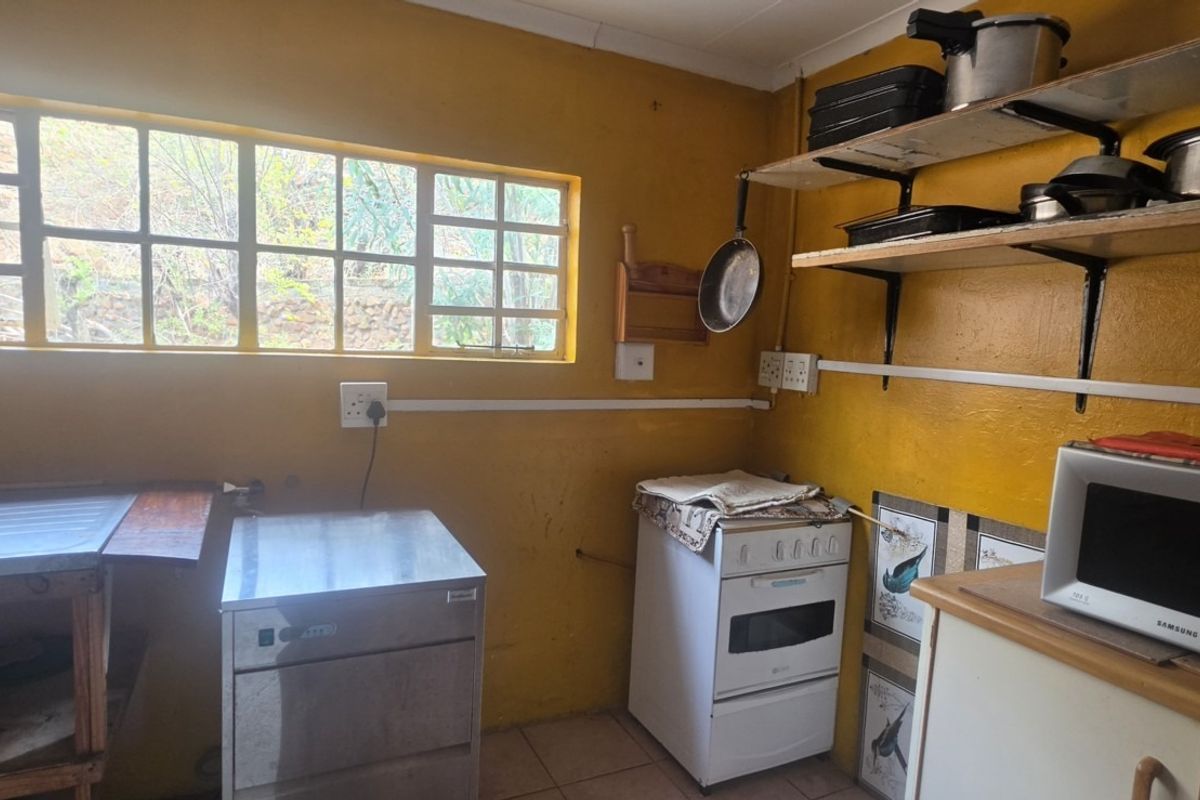 A functional kitchen area featuring a stainless steel sink, freestanding stove, and wall-mounted shelving, with potential for cosmetic updates to modernize the space.