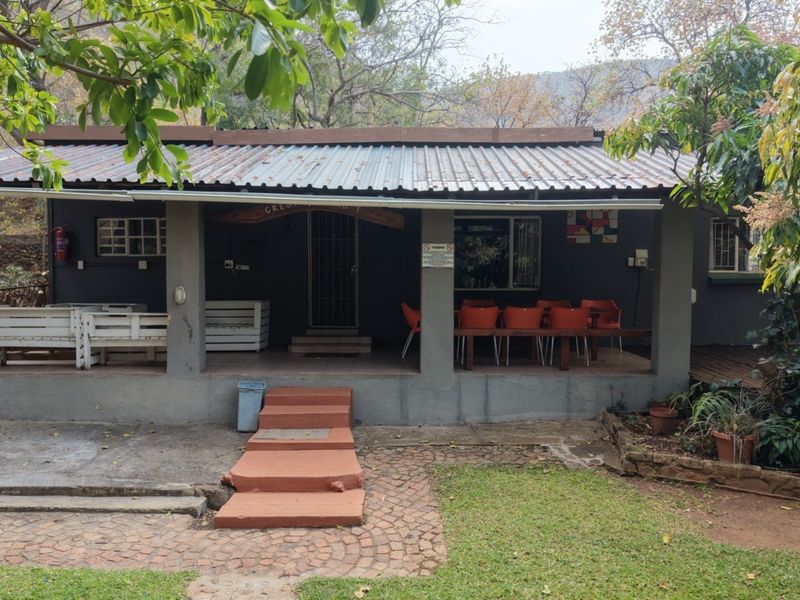 A covered outdoor patio area featuring a corrugated metal roof, concrete pillars, and brick steps leading to the main entrance of the farm building.