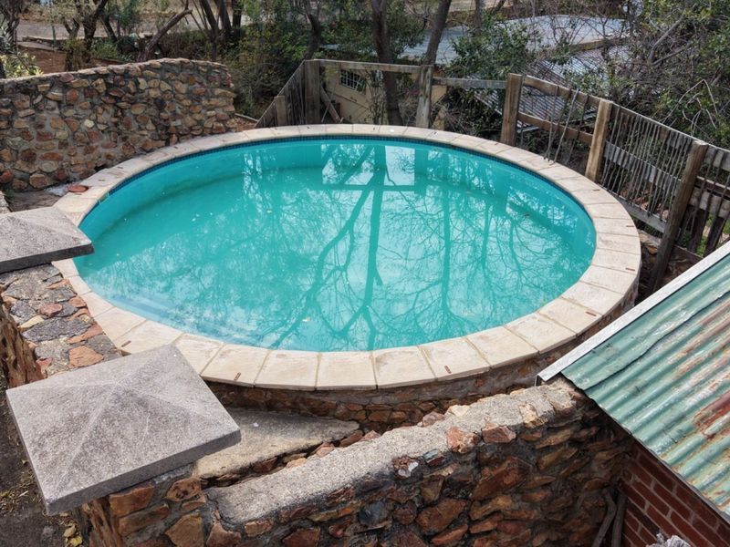 A circular swimming pool featuring stone retaining walls and concrete coping, set within a rustic outdoor area with timber fencing and corrugated metal roofing.