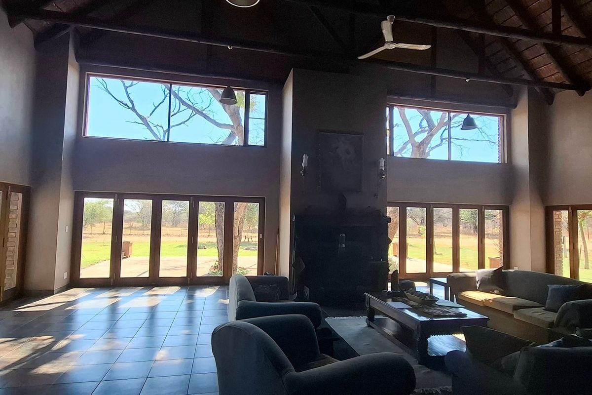Spacious living area featuring high vaulted timber ceilings, exposed trusses, tiled floors, and expansive glass stacker doors providing abundant natural light and garden views.