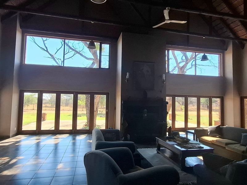 Spacious living area featuring high vaulted timber ceilings, exposed trusses, tiled floors, and expansive glass stacker doors providing abundant natural light and garden views.