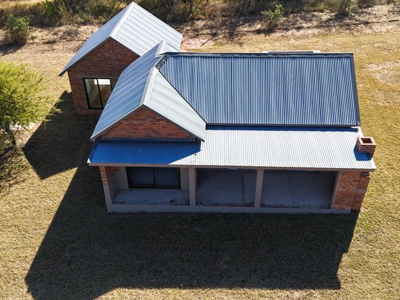 Aerial view of a farm-style residence featuring exposed brickwork, a corrugated metal roof, and an unfinished covered patio area set on a large plot.
