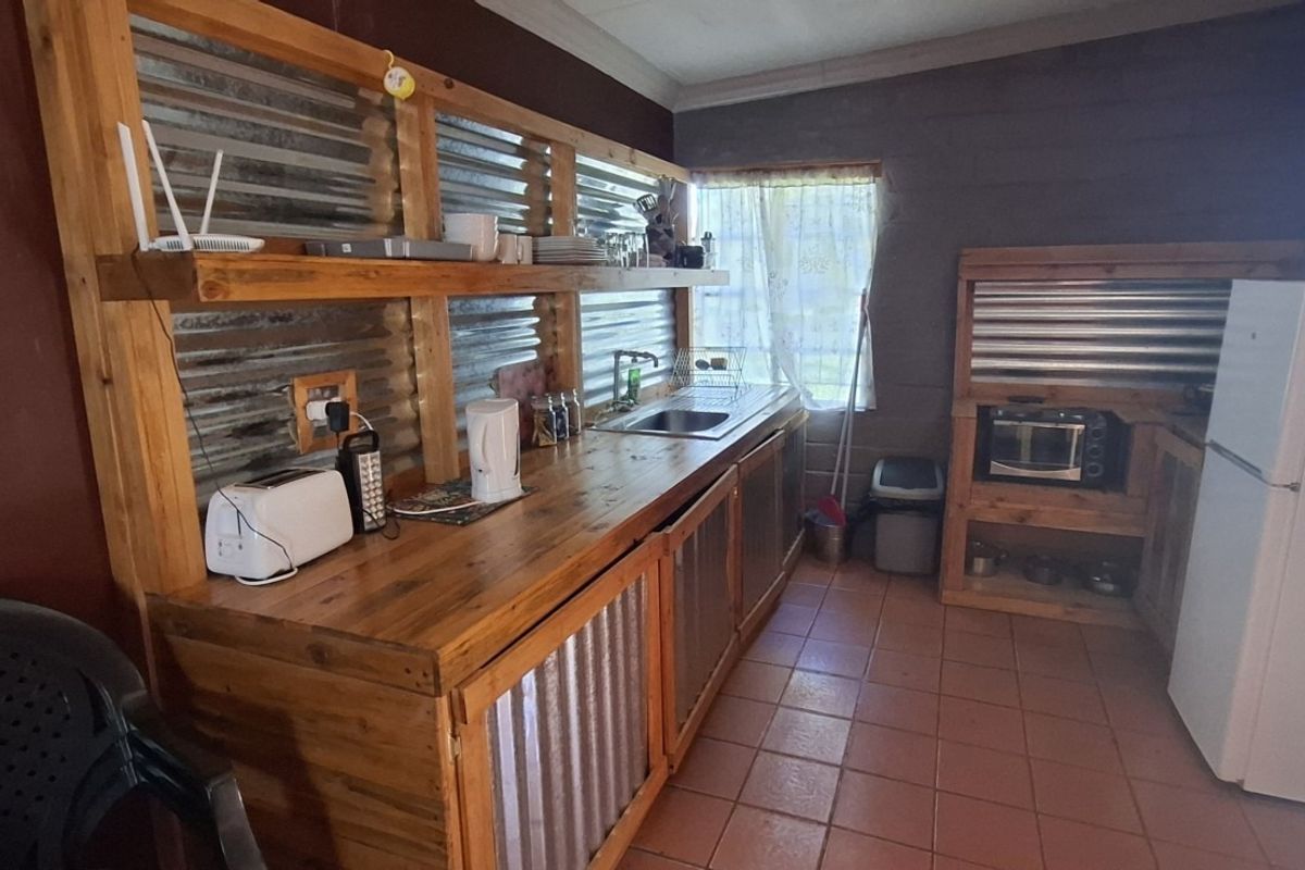 Rustic kitchen featuring custom timber cabinetry, corrugated metal accents, tiled flooring, and integrated shelving, offering a unique farm-style aesthetic.