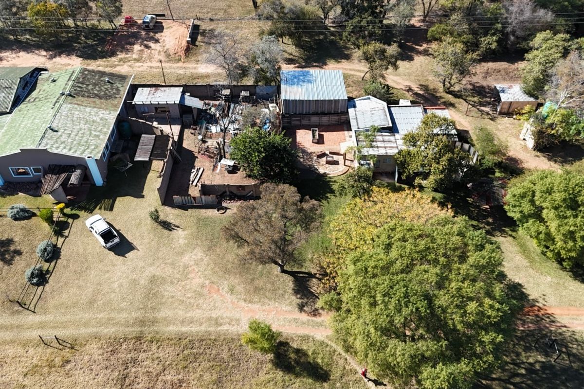 Aerial view of a farm property featuring multiple outbuildings, corrugated metal roofing, and expansive surrounding grounds.