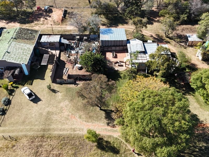 Aerial view of a farm property featuring multiple outbuildings, corrugated metal roofing, and expansive surrounding grounds.