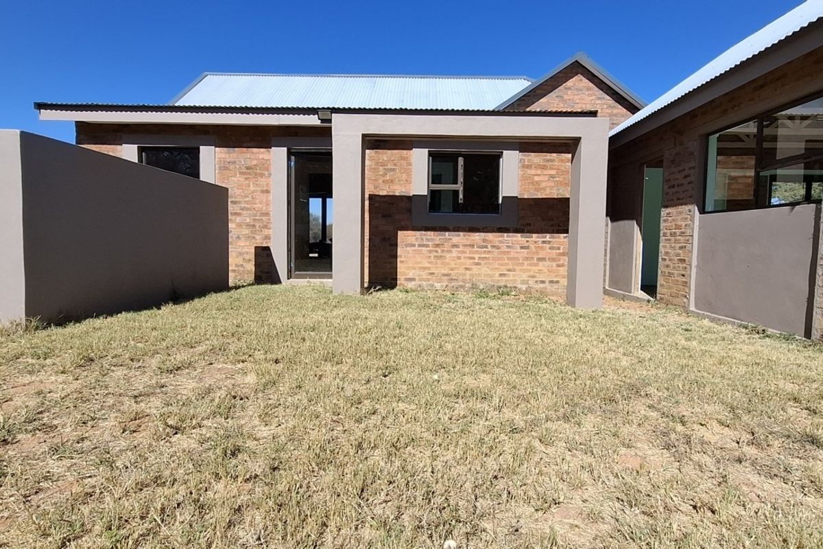 Rear view of a modern face brick farmhouse featuring a corrugated metal roof and aluminium window frames, set against a clear blue sky.
