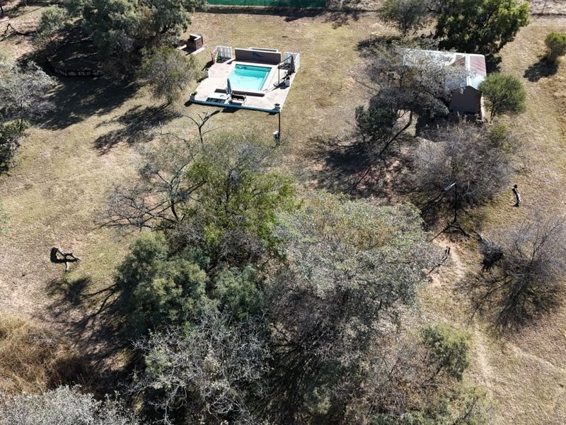 Aerial view of a farm property featuring a swimming pool with a surrounding deck and a small outbuilding set within a large, open landscape.