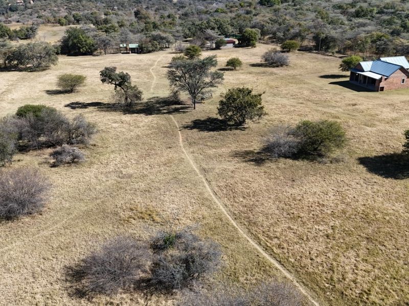 Aerial view of a rural farm property featuring a brick dwelling with a metal roof set within a large, open landscape.