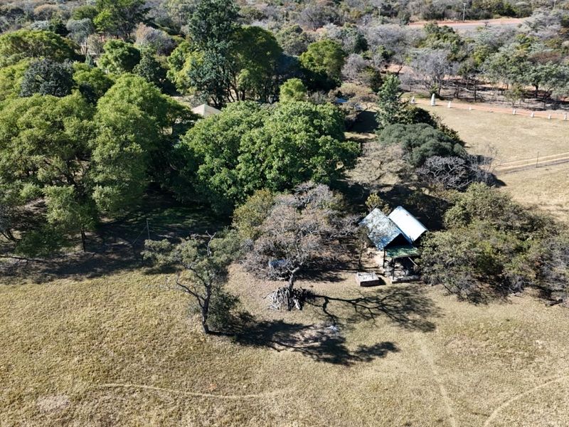 Aerial view of a rural farm property featuring a small structure with a corrugated metal roof surrounded by mature trees and open grazing land.