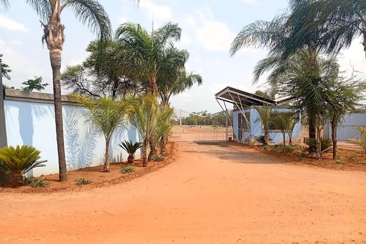 Front entrance view of the property featuring a perimeter wall, security gate, and a small guard house structure.
