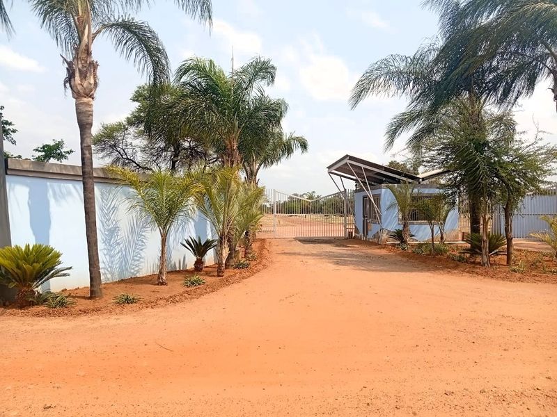 Front entrance view of the property featuring a perimeter wall, security gate, and a small guard house structure.