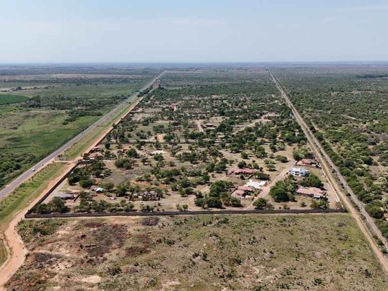 Aerial view of a large residential land plot featuring established vegetation, perimeter walling, and proximity to main road access.