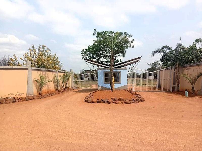 Front entrance view of a vacant residential property featuring a perimeter wall, security gate, and a central guard house structure.