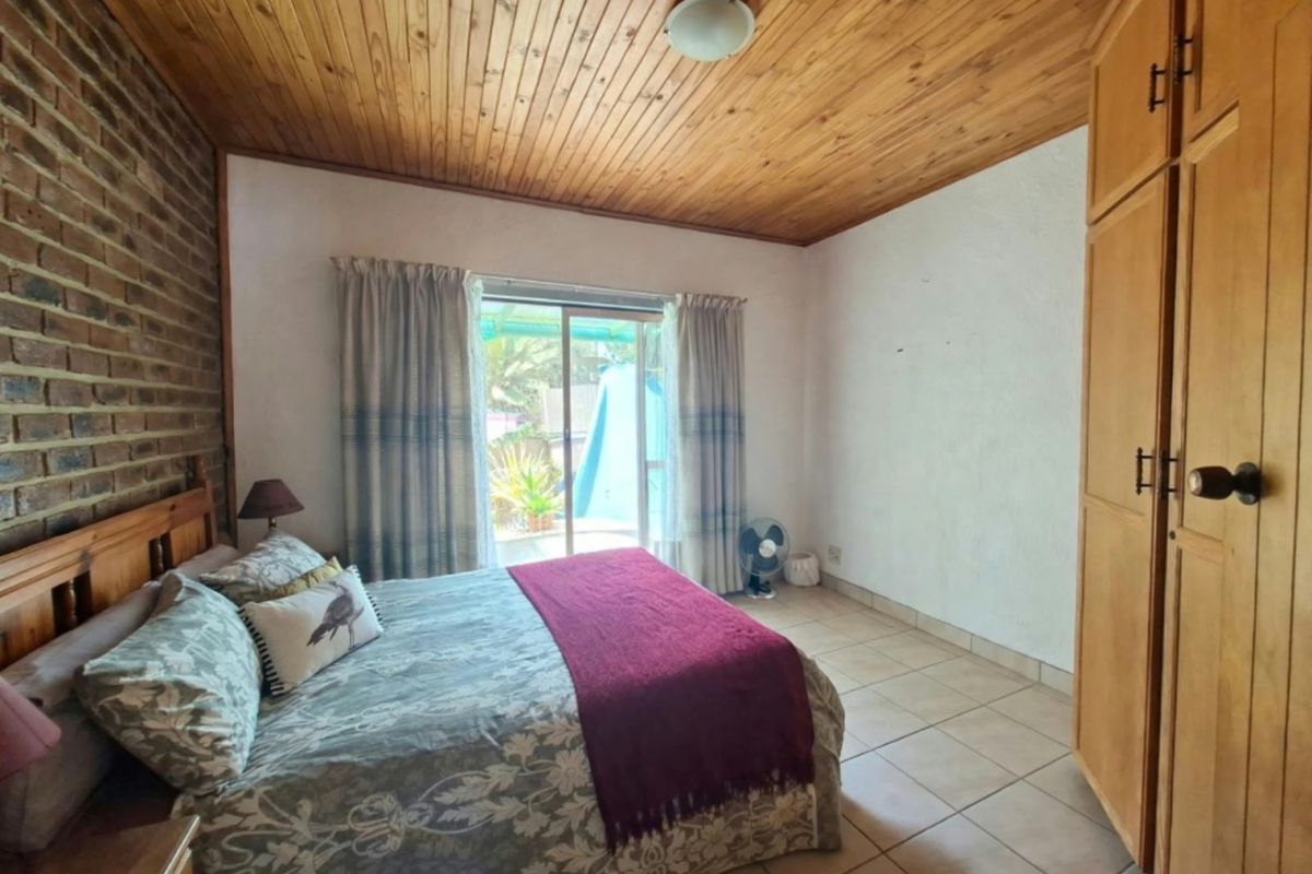 Bedroom featuring a timber ceiling, exposed brick feature wall, built-in wooden wardrobe, tiled flooring, and direct access to the outdoor area via sliding doors.