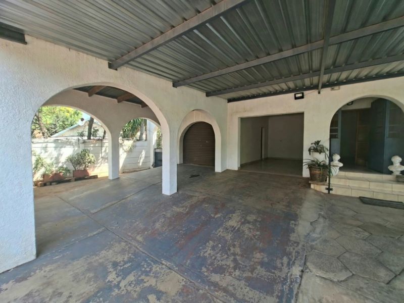 Covered front entrance and carport area featuring arched masonry pillars, a corrugated metal roof, and a paved driveway with a roller shutter garage door.