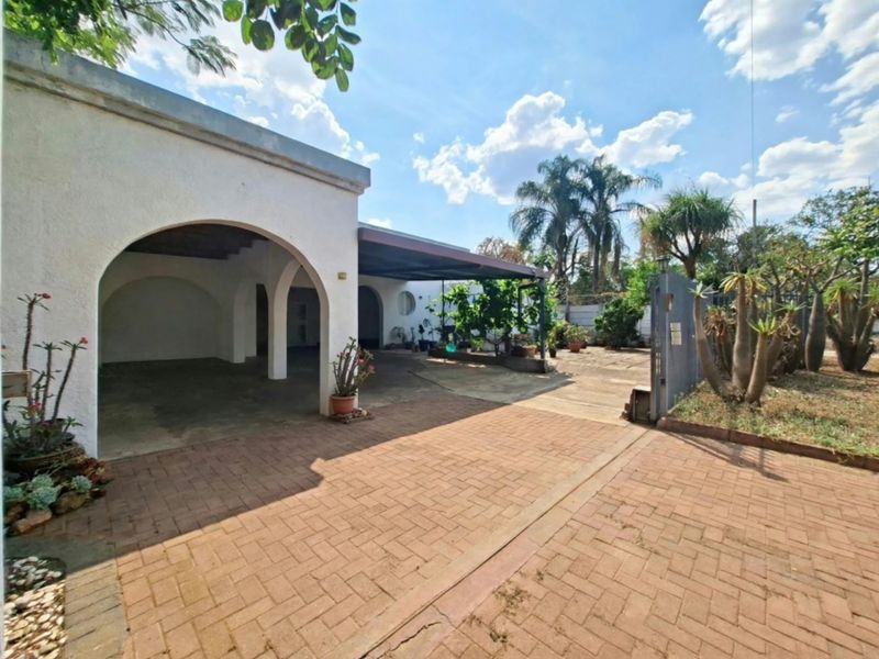 Front exterior view featuring a brick paved driveway, arched covered entrance, and a functional carport area with established garden surroundings.