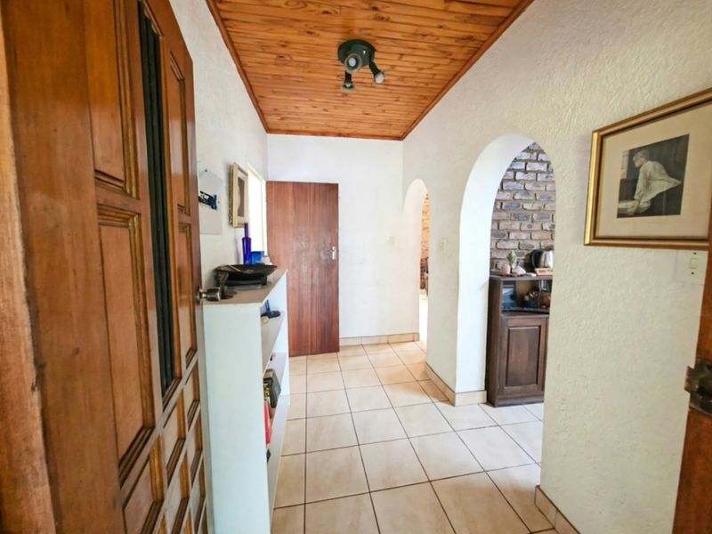 A bright hallway featuring a timber-clad ceiling, tiled flooring, and distinctive arched doorways leading into the living areas with an exposed brick feature wall.