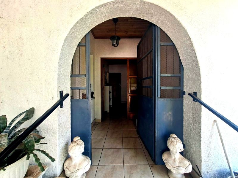 Entrance area featuring an arched doorway with metal security gates, tiled flooring, and a timber-paneled ceiling with a pendant light fixture.