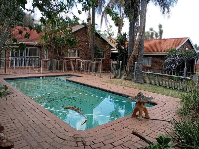 Outdoor pool area featuring a swimming pool with brick paving, metal fencing, and face brick house exterior.