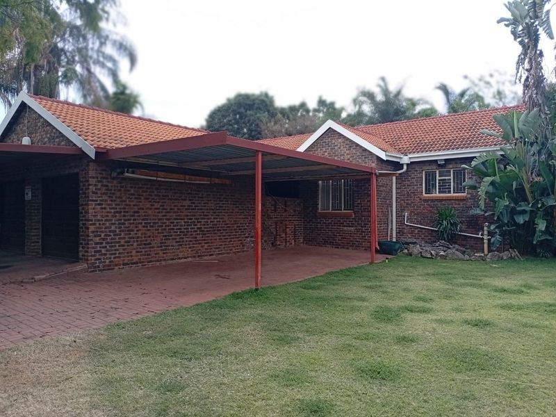 A brick-faced house exterior featuring a tiled roof, a covered carport, and a paved driveway area set against a lawn.