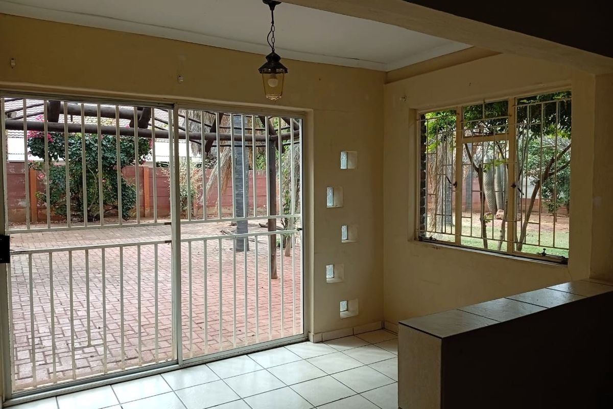 An empty living area featuring tiled flooring, a sliding glass door with security bars, and a built-in partition wall, overlooking a paved outdoor space.