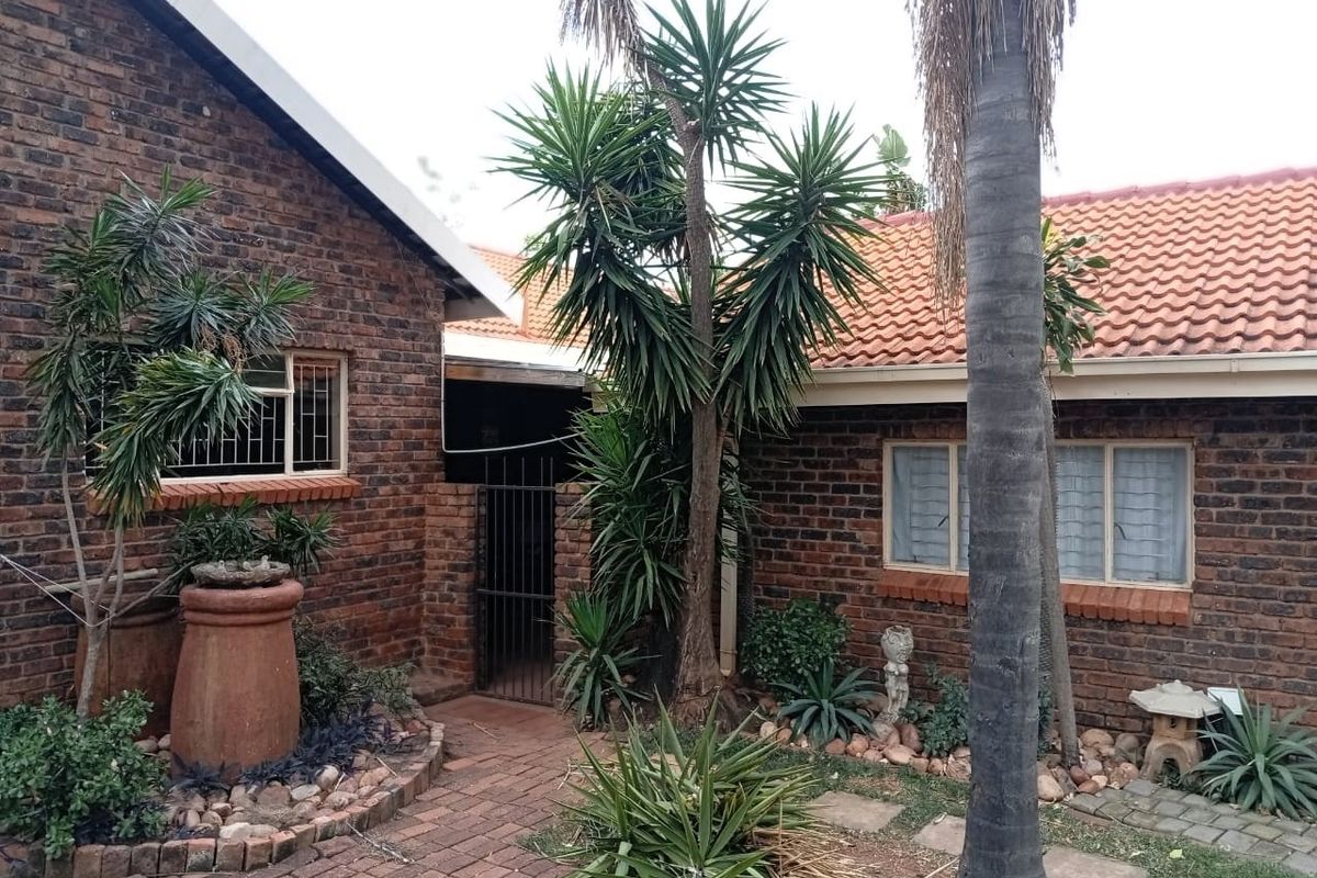 A rear exterior view of a face brick house featuring a tiled roof, security-barred windows, and a paved garden walkway.