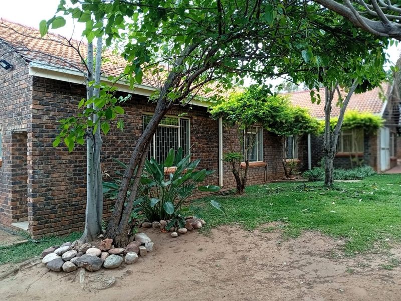 A view of the rear face brick facade of the house, featuring terracotta roof tiles, security-barred windows, and a mature garden setting.