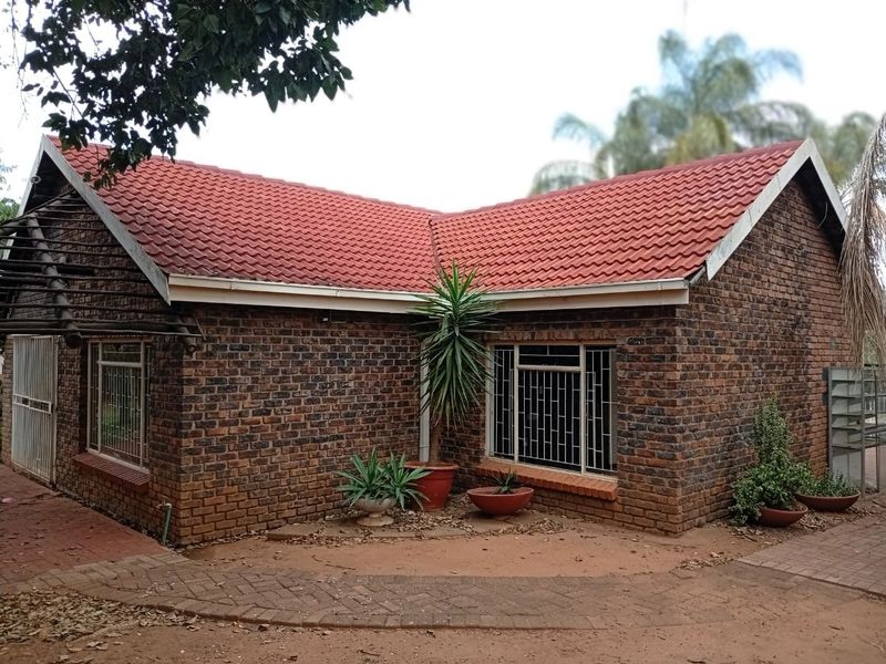 A charming face brick house featuring a distinctive red tiled roof, secure window bars, and a paved entrance area with a timber pergola.