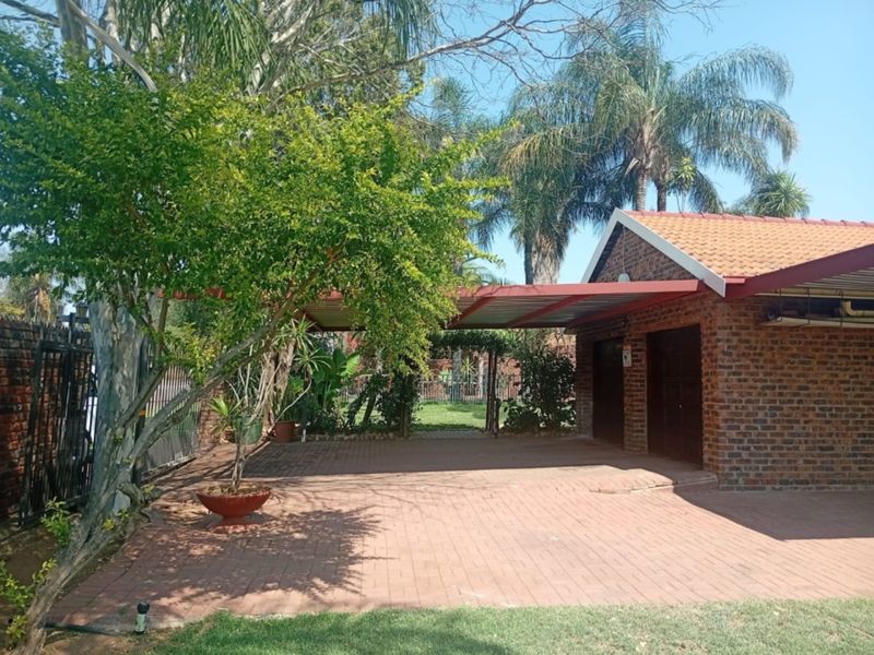 A rear exterior view featuring a brick garage structure with a tiled roof, a paved driveway, and a covered carport area.