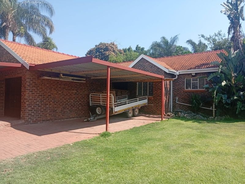Rear view of a face brick house featuring a covered carport, paved driveway, and a well-maintained garden area.
