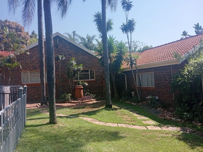Rear view of a face brick house featuring a tiled roof, established garden with paved pathways, and pool area fencing.
