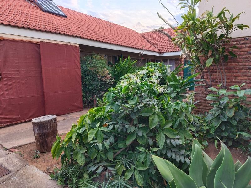 Rear exterior view of the property featuring a tiled roof with solar water heater, brick wall construction, and established garden area.