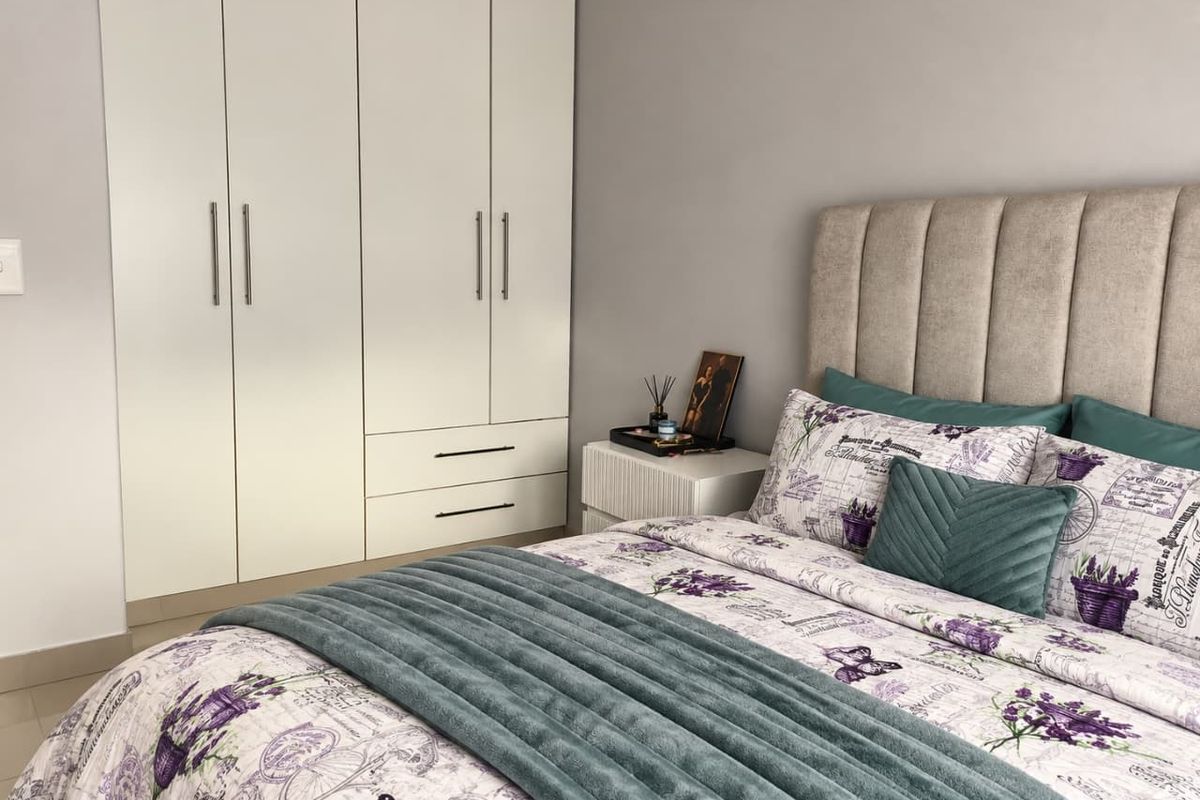 A well-maintained bedroom featuring a large white built-in wardrobe with integrated drawers and neutral tiled flooring.